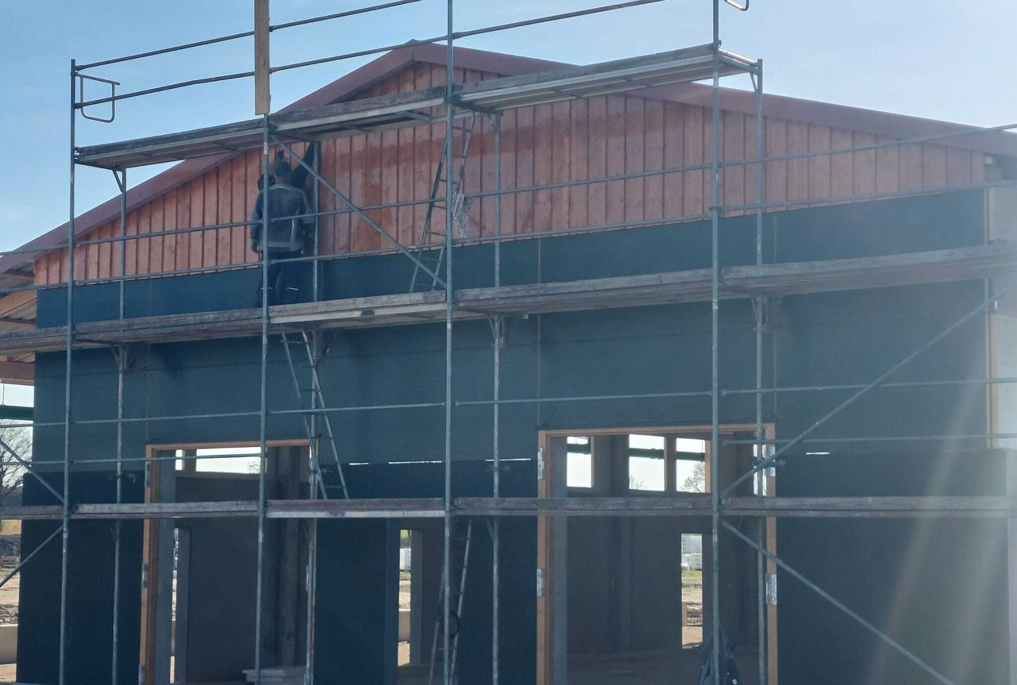 Handwerker montiert Fassadenverkleidung auf dem Gerüst einer Stallhalle
