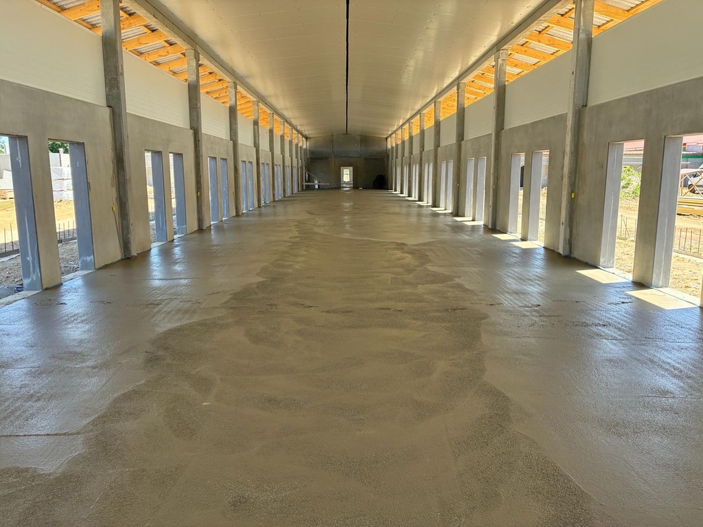 Fertiggestellte Stallhalle mit frisch geglättetem Betonboden und symmetrischer Holzdachkonstruktion