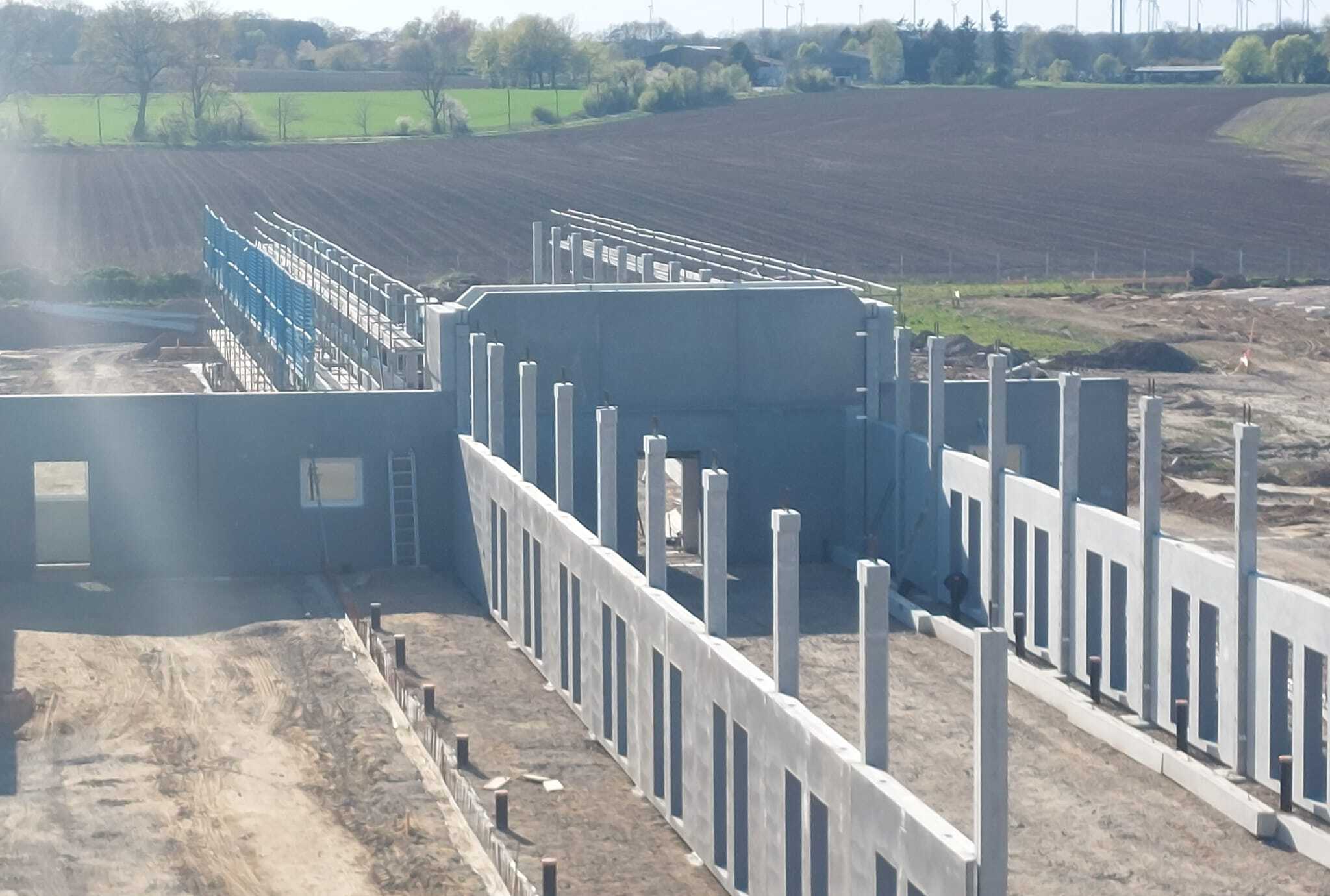 Luftaufnahme einer Baustelle mit vorgefertigten Betonwandelementen und Feldern im Hintergrund
